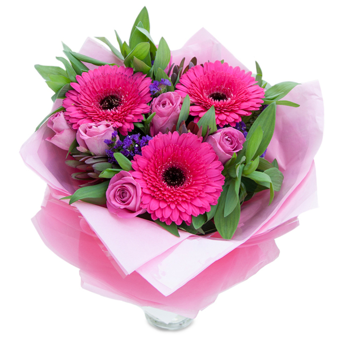 There is a playful grace to this bouquet: three striking fuchsia Gerbera daisies open wide, their concentric rows of petals leading the eye inward to bold dark centres that provide a dramatic contrast. Surrounding them, dusty-rose and lavender-pink roses curl into themselves with the soft, layered petals of early blooms, creating a gentle, romantic counterbalance to the Gerberas' exuberance. Interspersed throughout are sprigs of purple statice, their tiny clustered flowers offering flecks of cool violet and a papery texture that makes the arrangement feel almost wildflower-like. Rich green foliage-broad, slightly waxy salal leaves and the muted, fragrant silver of eucalyptus-envelops the bouquet, giving it a garden-fresh fullness and a pleasant leafy scent. The presentation is as considered as the floristry: the stems rest against a pale pink matte tissue inner layer, wrapped again in a gauzy fuchsia-pink cellophane that shimmers slightly and is artfully folded to cradle the blooms. A clear glass vase peeks out at the base, indicating the bouquet is intended for immediate display, ready to rest on a kitchen counter or bedside table. In the soft daylight of an early afternoon, the combination of hot pink, dusty rose and cool purple reads as both buoyant and refined. This bouquet feels suited to many moments-an anniversary at a favourite Kingston restaurant, a birthday surprise after a stroll by the riverside, or a simple gesture to remind someone they are cherished.